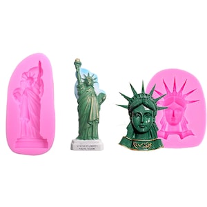 May include: The image features a green Statue of Liberty figurine, a green bust, and two pink silicone molds of the statue. The figurine has a white base with the text "Statue of Liberty New York". The bust has the word "NEWYORK" on the base.