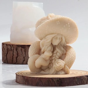 Puede incluir: Una escultura de cerámica blanca de una mujer con un sombrero de ala ancha y un chal. Ella sostiene un pequeño pájaro en su mano. La escultura está sentada sobre una base de madera.