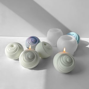 Può includere: Un set di sei candele bianche e viola a spirale, alcune con fiamme accese. Le candele sono rotonde e hanno una superficie testurizzata. Le candele sono disposte in cerchio su una superficie bianca.