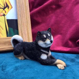 Puede incluir: Figura de perro Shiba Inu negro y blanco acostado sobre una superficie azul. La figura está detallada con pelo negro y marcas blancas.