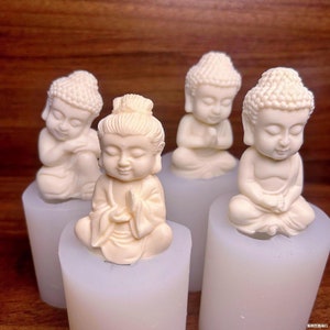May include: Four small white ceramic figurines of Buddha in various poses, sitting on white pedestals. The figurines are detailed with intricate hair and clothing.