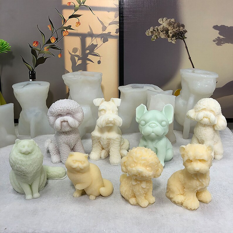 May include: A collection of nine white, beige, and green animal-shaped candles, including a cat, a poodle, a schnauzer, a bulldog, and a variety of other dog breeds. The candles are sitting on a white surface.