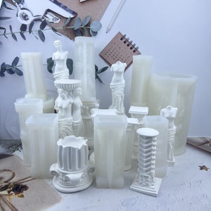 Pu&ograve; includere: Una collezione di stampi in gesso bianco per l'artigianato. Gli stampi sono a forma di colonne, piedistalli e statue di donne. Gli stampi sono disposti su una superficie bianca.