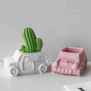 Może przedstawiać: Dwa miniaturowe doniczki w kształcie samochodów, jedna biała z zieloną rośliną kaktusową i jedna różowa.