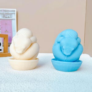 Peut inclure: Deux sculptures de serpents en céramique, l'une blanche et l'autre bleu clair, enroulées dans un bol. Les bols sont de la même forme, mais le bol blanc est blanc et le bol bleu est bleu clair.