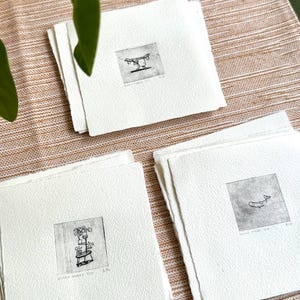 Peut inclure: Trois estampes en noir et blanc sur papier blanc. Chaque estampe présente un dessin au trait simple d'une plante. Les estampes sont intitulées "Black Garden" et numérotées 1/10, 2/10 et 3/10.