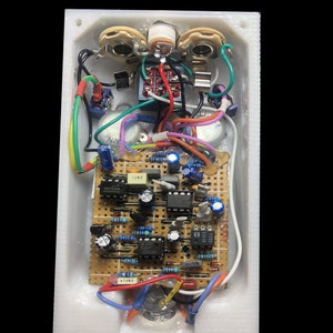 Op de afbeelding: Een witte rechthoekige behuizing met elektronische componenten. De printplaat heeft weerstanden, condensatoren en ge&iuml;ntegreerde schakelingen. De tekst "PRODUCT EXAMPLE" en "COMPONENTS NOT INCLUDED" zijn zichtbaar.