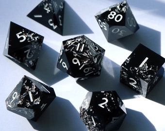 May include: Set of seven black dice with white numbers and a marbled effect. The dice are a d4, d6, d8, d10, d%, d12, and d20.