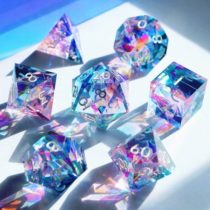 May include: Set of seven iridescent dice with a rainbow effect. The dice are made of clear plastic with a holographic finish. The numbers on the dice are visible and easy to read. The dice are perfect for tabletop gaming.