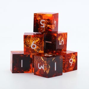 May include: A set of seven orange resin dice with gold foil inclusions. Each die has white numbers. The dice are stacked in a pyramid shape against a white background. The dice are cube-shaped.