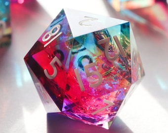 May include: A multi-faceted iridescent dice with the numbers 1, 2, 5, 8, 12, 15, and 18 printed on its faces. The dice is made of clear plastic with a rainbow effect.