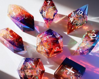 May include: Set of seven iridescent dice with a rainbow color gradient. The dice are made of clear resin with embedded glitter and have white numbers. The dice are shaped like a d4, d6, d8, d10, d%, d12, and d20.