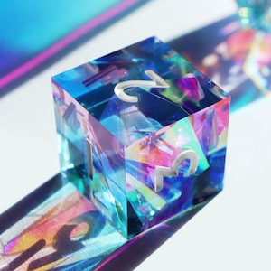 May include: A iridescent blue, green, and pink dice with the number 2 on one side and the number 3 on another side.