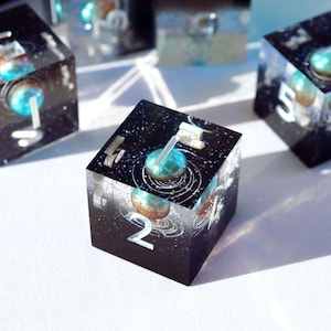 May include: Black resin dice with a galaxy design, featuring a blue and brown planet-like sphere. The dice have white numbers and are designed for tabletop games. The dice are cube-shaped and have a glittery effect.