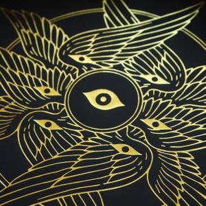 May include: A black background with a gold design of four stylized wings with eyes surrounding a central eye. The design is reminiscent of a mystical or spiritual symbol.