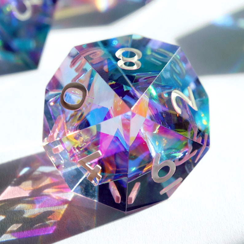 May include: A iridescent, multi-faceted, clear, glass d20 dice with silver numbers 1, 2, 4, 6, 8, 10, 12, 14, 16, 18, 20.