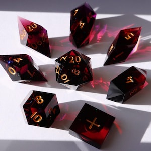 May include: Set of eight red and purple dice with gold numbers. The dice are in various shapes, including a d20, d12, d10, d8, d6, and d4.