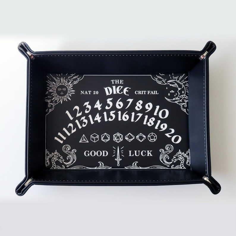 May include: Black leather dice tray with a white design featuring the words "The Dice", "Nat 20", "Crit Fail", "Good Luck", and numbers 1-20. The tray has a sun and moon design on either side.