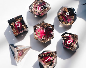 May include: Set of six polyhedral dice with gold leaf and dried flower accents. The dice are clear with a dark background and white numbers. The dice are in various shapes, including a d4, d6, d8, d10, d12, and d20.