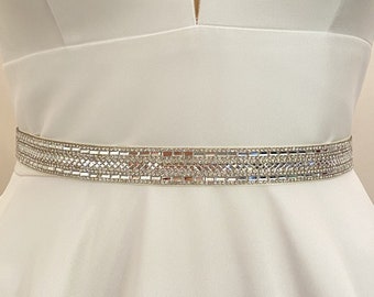 May include: A white satin wedding dress with a V-neckline and a sparkling rhinestone belt.