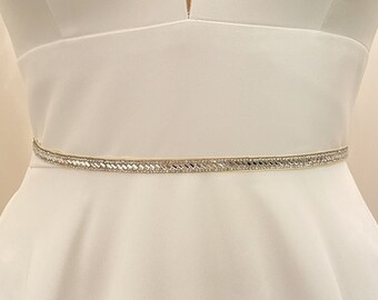 May include: A white satin wedding dress with a V-neckline and a thin, beaded belt.
