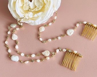 May include: A gold hair comb with a white flower and pearl chain. The chain is adorned with small pearls and rhinestones. The comb is a bridal hair accessory.