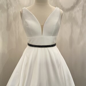 May include: A white sleeveless dress with a deep V-neckline and a black rhinestone belt.