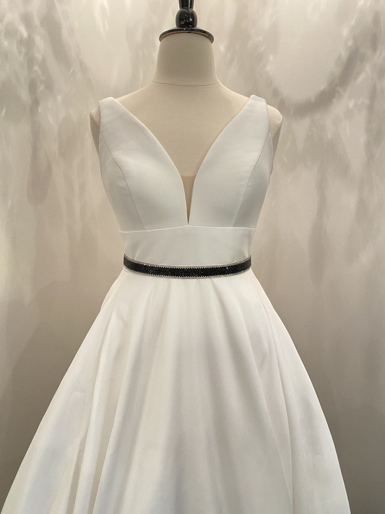May include: A white sleeveless dress with a deep V-neckline and a black rhinestone belt.