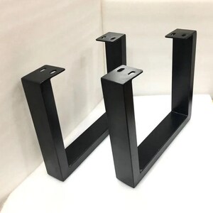 May include: Two black metal table legs in a U-shape design. Each leg has a flat top with pre-drilled holes for easy attachment. The legs are made of sturdy metal and are suitable for various furniture projects.
