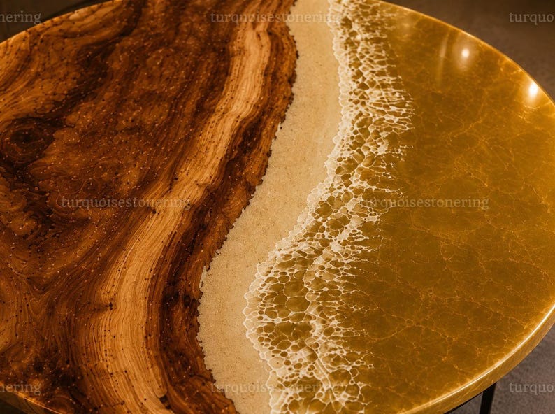 Puede incluir: Una mesa redonda con una losa de madera natural con vetas prominentes en un lado, que transiciona hacia una franja de arena texturizada y una secci&oacute;n de resina dorada transl&uacute;cida que imita olas con detalles de espuma blanca.