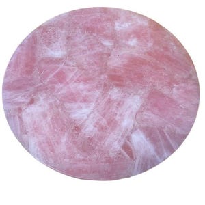 May include: A circular rose quartz stone, polished to a smooth finish. The stone is a delicate pink hue, featuring white veining that creates a mosaic effect. The overall appearance is natural and organic, with a reflective surface.