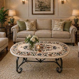 May include: Oval coffee table with a cream-colored marble top featuring a floral mosaic design in shades of red, blue, and green. The table has a black wrought iron base and sits on a cream-colored rug. The table is surrounded by beige furniture.