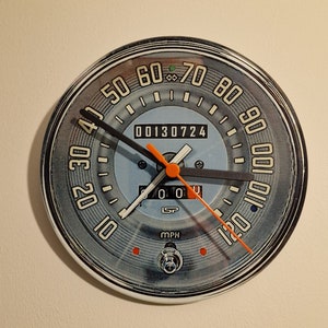 May include: A vintage-style speedometer clock with a blue face and silver trim. The clock face has black hands and orange numbers. The clock reads 00130724 and has the text "SP" and "MPH".