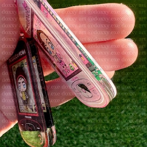 May include: Two acrylic keychains shaped like retro mobile phones. One is pink with a cartoon character and the text 'Jesse', the other is black with a cartoon character and the text 'Pinkman'. Both feature digital screen graphics and buttons.
