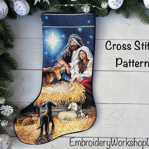 Pode incluir: Uma meia de Natal com um padrão detalhado de ponto cruz de uma cena de natividade com uma estrela brilhante, figuras e animais num fundo azul escuro. O texto Cross Stitch Pattern e EmbroideryWorkshopLV são visíveis na imagem.