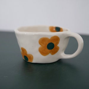 May include: A white ceramic mug with a handle, decorated with three orange and green flowers.