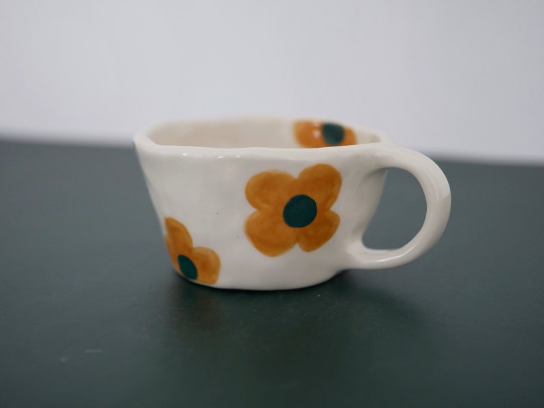 May include: A white ceramic mug with a handle, decorated with three orange and green flowers.