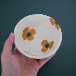 May include: A white ceramic bowl with a floral design. The bowl has three brown flowers with green centres.