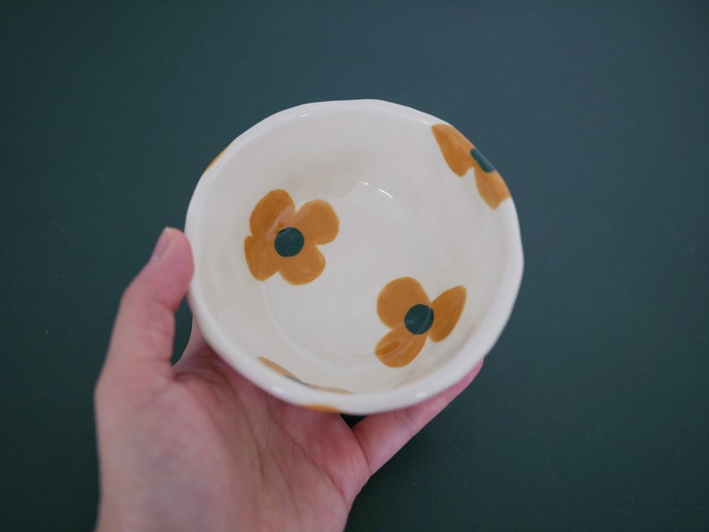 May include: A white ceramic bowl with a floral design. The bowl has three brown flowers with green centres.
