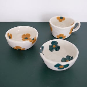 May include: Three ceramic bowls with floral designs. The bowls are white with yellow and green flowers. The bowls are of different sizes.