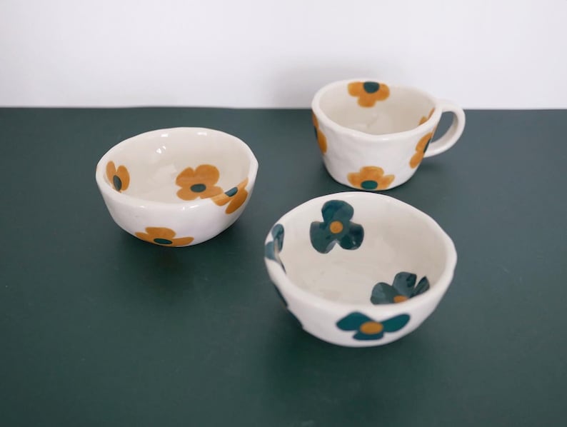 May include: Three ceramic bowls with floral designs. The bowls are white with yellow and green flowers. The bowls are of different sizes.