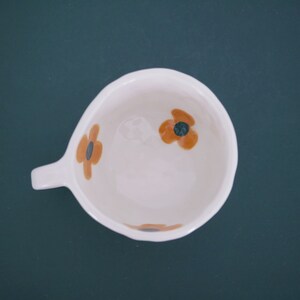 May include: White ceramic mug with a handle and three orange and brown floral designs.