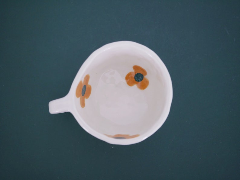 May include: White ceramic mug with a handle and three orange and brown floral designs.