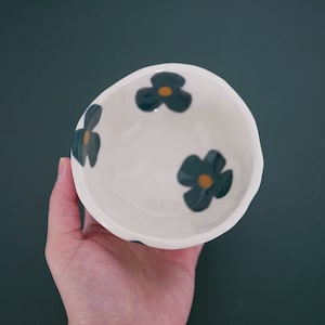 May include: A white ceramic bowl with a blue and yellow floral design. The bowl is empty and has a slightly uneven rim.