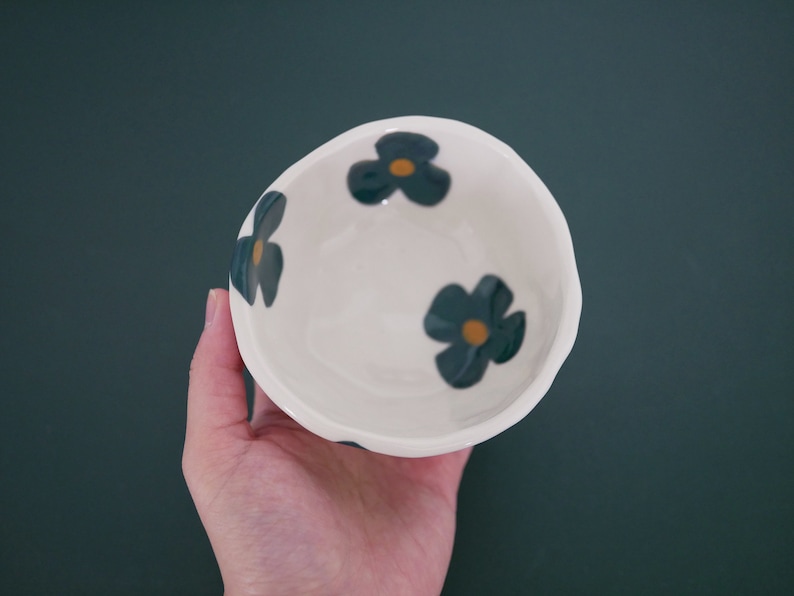 May include: A white ceramic bowl with a blue and yellow floral design. The bowl is empty and has a slightly uneven rim.