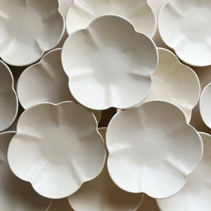 May include: A set of ten off-white ceramic bowls with a scalloped edge. The bowls are arranged in a circular pattern.