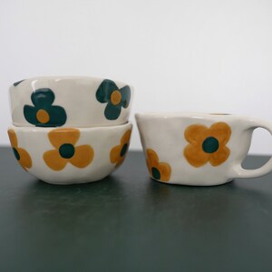 May include: Three white ceramic bowls with a floral pattern. The bowls have a yellow and green flower design. The bowls are stacked on top of each other.