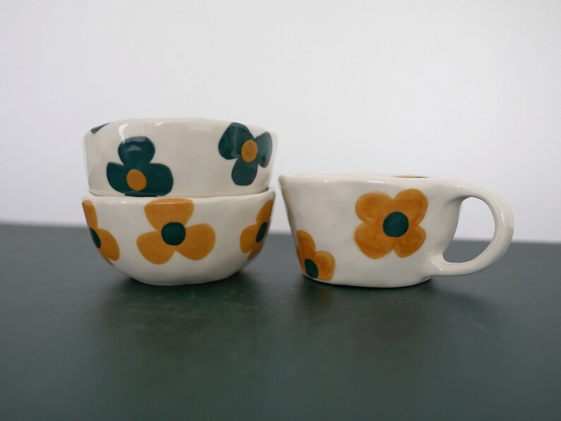 May include: Three white ceramic bowls with a floral pattern. The bowls have a yellow and green flower design. The bowls are stacked on top of each other.