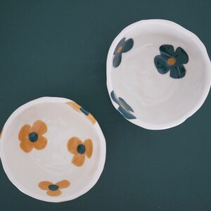 May include: Two white ceramic bowls with floral designs. One bowl has blue and yellow flowers, the other has yellow and black flowers.