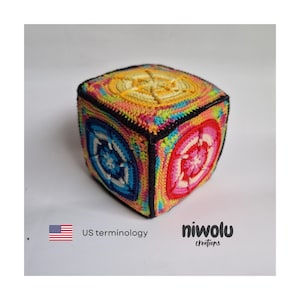 May include: A crocheted cube with vibrant colors, including yellow, pink, blue, and green. Each side features a unique circular design. The cube has a black border and is set against a white background. The text "niwolu creations" is visible.